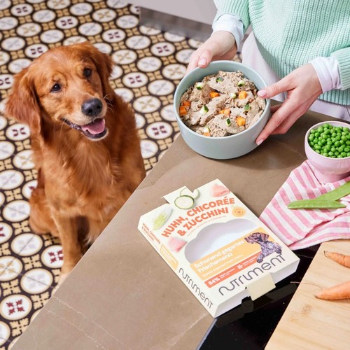 Nutriment Fresh | Vers Hondenvoer, 5 smaken 3 Verpakking Nutriment Fresh naast een gevulde voerbak op het aanrecht, met een wachtende hond ernaast